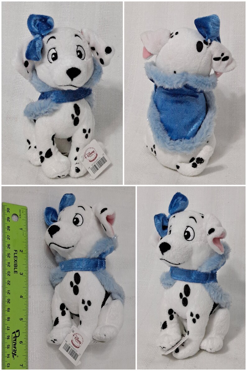 May include: A white and black Dalmatian plush toy wearing a blue and white fur-trimmed scarf and a blue bow. The plush toy is sitting with its legs tucked underneath it. The toy has a Disney Store tag attached to it.