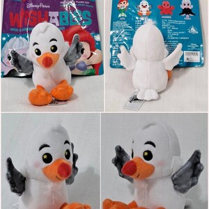 May include: A white plush toy seagull with orange feet and black wings. The seagull is sitting with its wings spread out. The toy is part of the Disney Pixar Wishables collection.