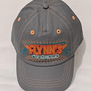 May include: Gray baseball cap with orange stitching and a button on top. The front features the text "FLYNN'S TOP SCORE CLUB" in orange and teal, with a retro video game design. A stylish accessory.