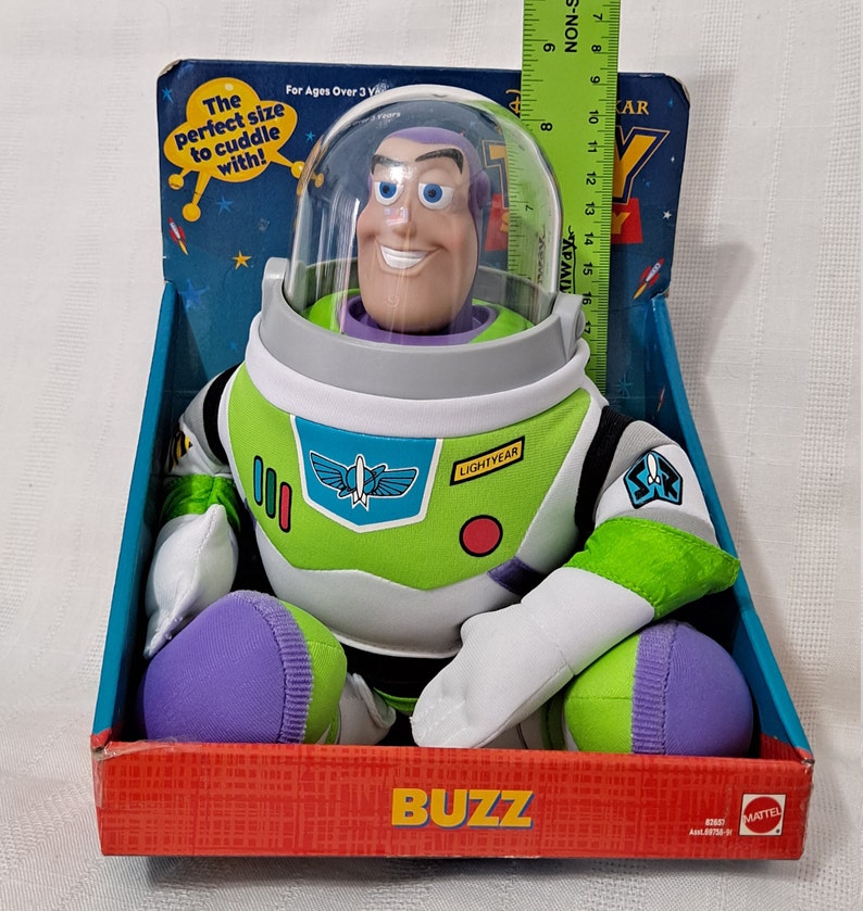 K&ouml;nnte beinhalten: Ein Pl&uuml;sch-Buzz Lightyear Spielzeug aus der Toy Story-Reihe. Das Spielzeug sitzt in einer Schachtel mit den Worten "Buzz" und "Lightyear" darauf. Das Spielzeug tr&auml;gt einen gr&uuml;n-wei&szlig;en Raumanzug mit einem violetten Helm. Das Spielzeug ist f&uuml;r Kinder ab 3 Jahren geeignet.