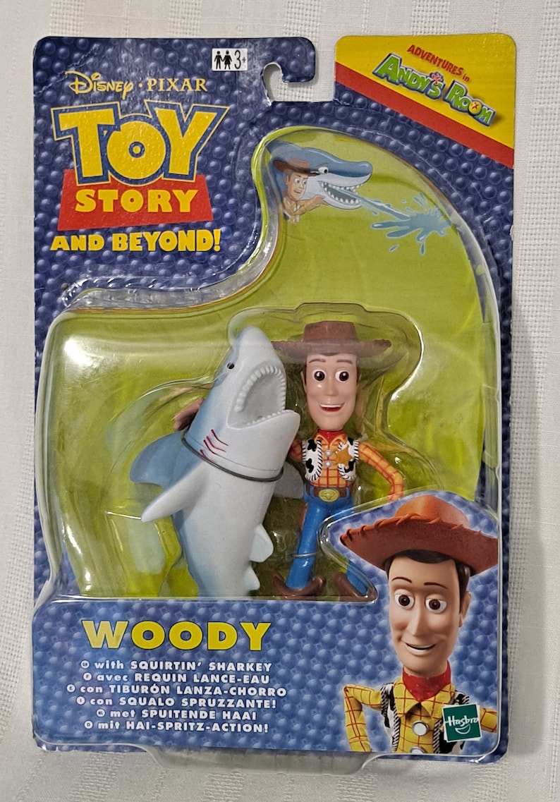 May include: Woody from Toy Story action figure with a water squirting shark toy. The packaging features the text "Adventures in Andy's Room" and "Toy Story and Beyond!"