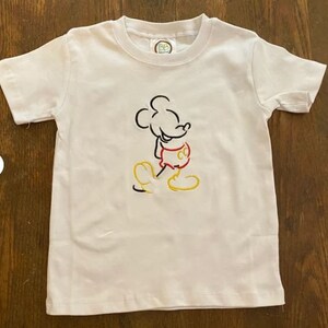 Op de afbeelding: Wit T-shirt met een zwarte en rode geborduurde omtrek van Mickey Mouse.