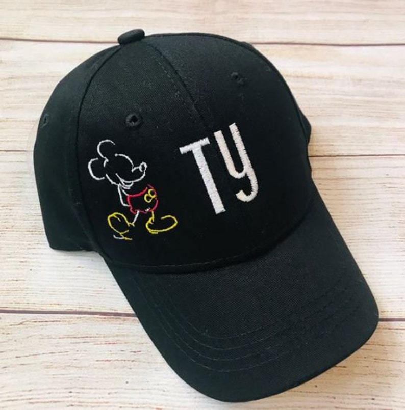 Op de afbeelding: Zwarte baseballpet met een witte geborduurde Mickey Mouse en de naam "TY" in wit.