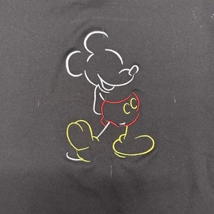 Op de afbeelding: Zwart geborduurd T-shirt met een witte omtrek van Mickey Mouse die een rode broek draagt met de letters "CC" erop.