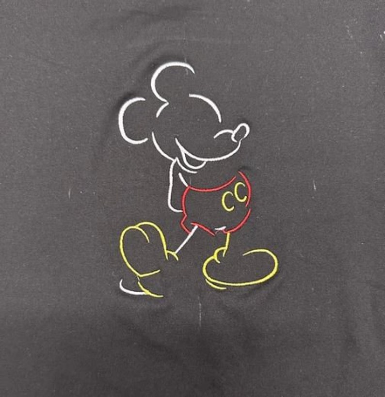 Op de afbeelding: Zwart geborduurd T-shirt met een witte omtrek van Mickey Mouse die een rode broek draagt met de letters "CC" erop.