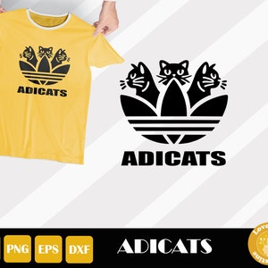 May include: Yellow t-shirt with a black graphic featuring three cat faces within a stylized design, and the word "ADICATS" below. The shirt has a white collar and short sleeves.