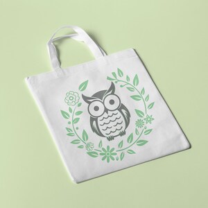Puede incluir: Bolsa de tela blanca con un dise&ntilde;o de b&uacute;ho blanco y negro rodeado de hojas y flores verdes.