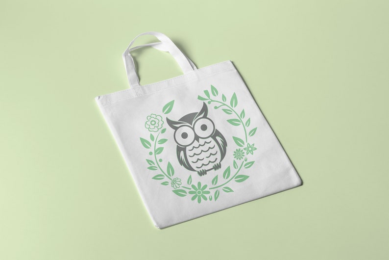 Puede incluir: Bolsa de tela blanca con un dise&ntilde;o de b&uacute;ho blanco y negro rodeado de hojas y flores verdes.
