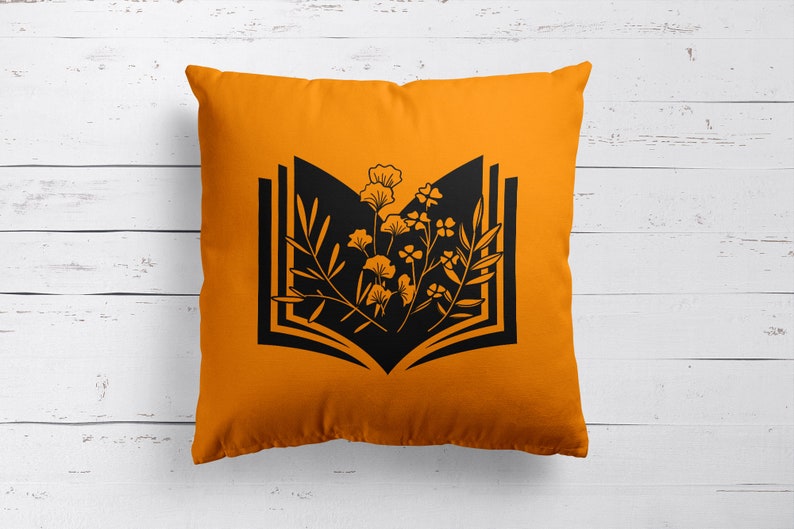 May include: Orange throw pillow with a black silhouette of an open book with flowers growing out of it.