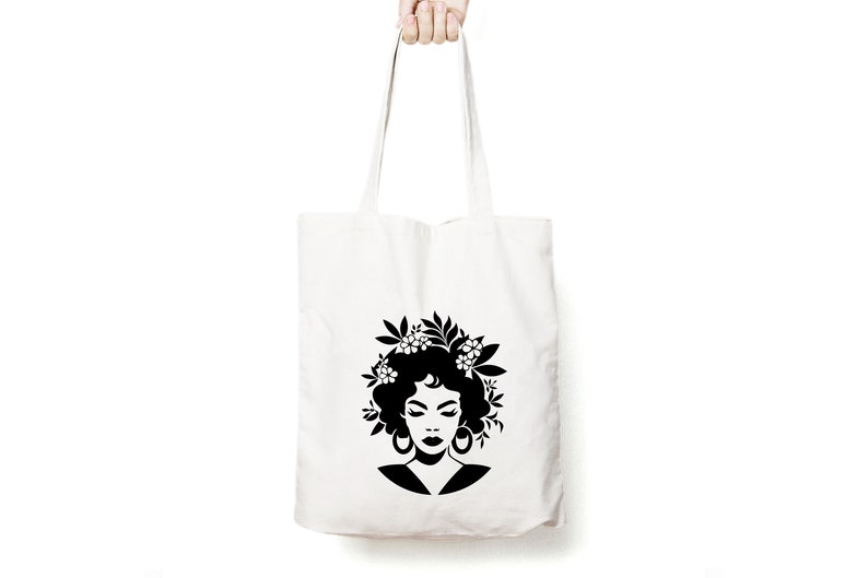May include: A white tote bag with a black silhouette of a woman with flowers in her hair. The woman is wearing large earrings.