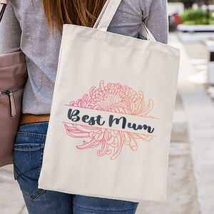 以下が含まれることがあります： 濃い青色の「Best Mum」の文字と、ピンクとオレンジの花柄が描かれた白いトートバッグです。