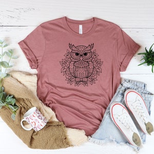 Puede incluir: Una camiseta color malva con un gr&aacute;fico en blanco y negro de un b&uacute;ho con detalles intrincados. El b&uacute;ho est&aacute; rodeado de un dise&ntilde;o floral.