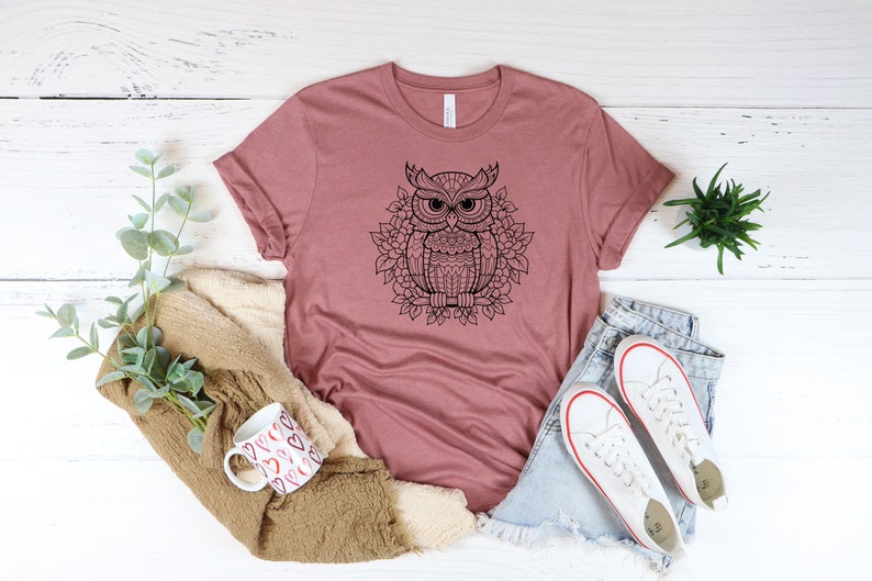Puede incluir: Una camiseta color malva con un gr&aacute;fico en blanco y negro de un b&uacute;ho con detalles intrincados. El b&uacute;ho est&aacute; rodeado de un dise&ntilde;o floral.