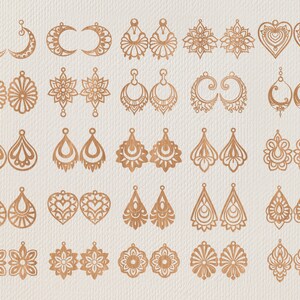 May include: A collection of various laser-cut earrings in a warm, metallic tone. Designs include crescent moons, floral patterns, teardrops, and hearts. The earrings are displayed on a neutral, textured background.