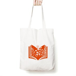 May include: A white tote bag with orange handles and a design of an open book with flowers inside.