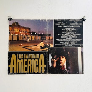 May include: A vintage film poster for the movie "Once Upon a Time in America" featuring a scene from the film with a man in a hat and a cityscape in the background. The poster is in Italian and features the title "C'era una volta in America" in gold lettering.