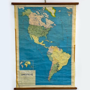 May include: Vintage map of the Americas, featuring North and South America, with a blue ocean background. The map is mounted on wooden rods for hanging. The text "ΑΜΕΡΙΚΗΣ" is visible at the bottom.