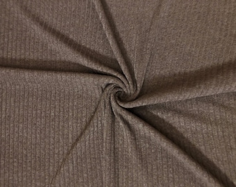 May include: Close-up of a brown ribbed knit fabric. The fabric is folded and swirled, showing the texture and direction of the knit. The color is a muted brown, with subtle variations in tone.