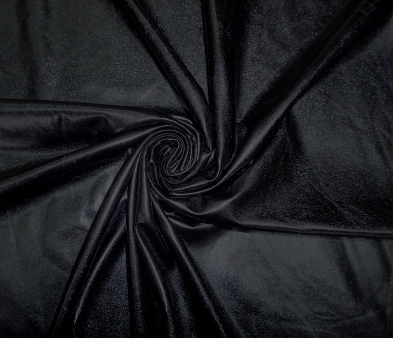 May include: Black fabric with a smooth, silky texture. The fabric is draped and folded to create a swirling pattern.