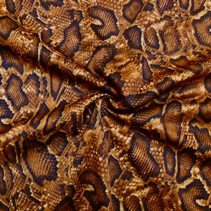 May include: A fabric featuring a repeating snake skin pattern in shades of brown, tan, and black. The material is gathered in the center, creating folds and shadows that highlight the textured appearance of the printed reptilian scale design.