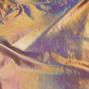 May include: Close-up of iridescent fabric with a gold, purple and blue colour scheme. The fabric is wrinkled and has a soft, silky texture.
