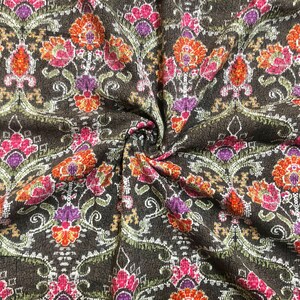 May include: Close-up of a brown fabric with a repeating floral pattern. The flowers are in shades of pink, orange, and purple. The fabric has a textured surface.