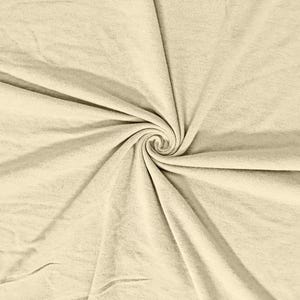 May include: A close-up of a cream-colored fabric with a spiral pattern in the center. The fabric has a soft, textured appearance with visible folds and creases. The overall tone is neutral and warm.
