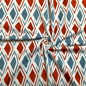 May include: White fabric with a repeating geometric pattern of red and blue diamonds. The fabric is folded and textured.