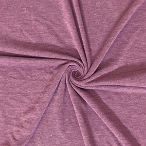 May include: A close-up shot of a swirl of mauve fabric. The fabric has a soft, heathered texture, with subtle variations in color. The fabric is gathered in a spiral, creating a focal point in the center of the image. The fabric is likely used for clothing or home decor.