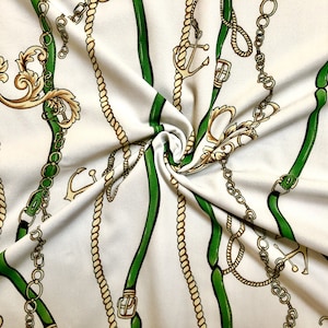 May include: White fabric with a repeating pattern of gold chains, green ropes, and anchors. The fabric is folded and draped.