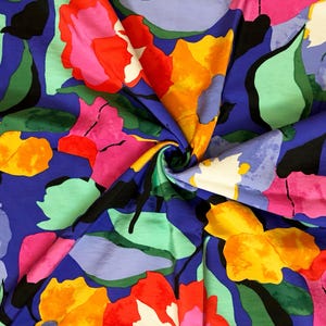 Puede incluir: Una tela vibrante con un estampado floral. El diseño presenta grandes flores abstractas en tonos de rosa, amarillo, naranja y morado, sobre un fondo azul oscuro. Hojas verdes y acentos negros completan la colorida composición.