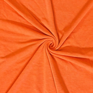Könnte beinhalten: Nahaufnahme eines leuchtend orangefarbenen Stoffes, der eng spiralförmig gewirbelt ist. Das Material wirkt weich und strukturiert, mit sichtbaren Falten und Schatten, die die Tiefe und den Fall des Stoffes betonen. Die Farbe ist durchgängig.