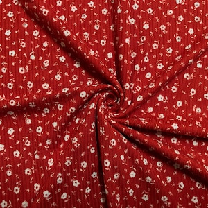 May include: Red ribbed fabric with a white floral pattern. The fabric is textured and has a soft, drapey feel.