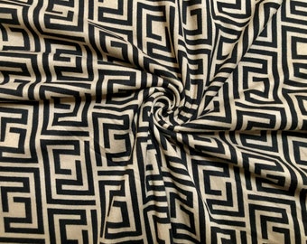 May include: Beige fabric with a black geometric pattern of interlocking squares and rectangles. The fabric is folded and draped, creating a swirling effect.