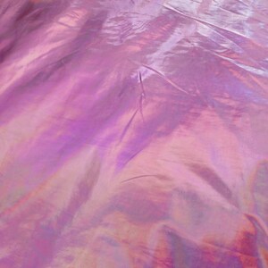 May include: Close-up of iridescent fabric with a pink and purple hue. The fabric has a smooth, silky texture and is slightly wrinkled.