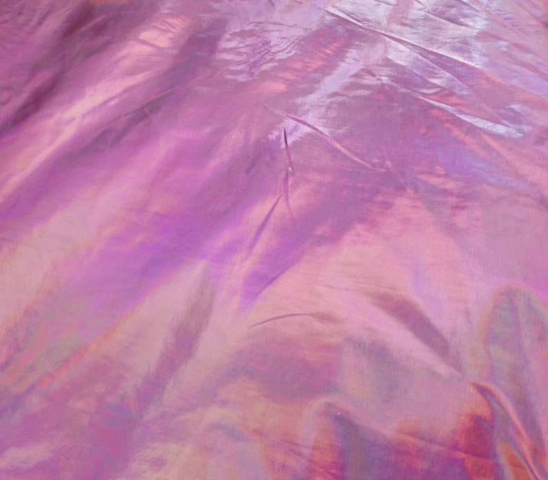 May include: Close-up of iridescent fabric with a pink and purple hue. The fabric has a smooth, silky texture and is slightly wrinkled.