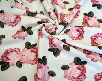May include: White fabric with a pink rose floral print. The fabric is soft and has a subtle texture.