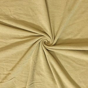 May include: Close-up of a golden-yellow fabric with a soft texture. The material is swirled into a spiral, creating folds and shadows that highlight its drape and texture. The fabric appears to be a knit or jersey material.