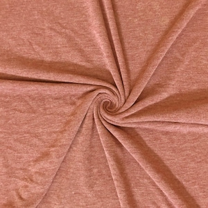 May include: Close-up of a swirl of soft, textured fabric in a muted reddish-brown hue. The fabric is gathered in a spiral, showcasing its drape and subtle variations in color. Ideal for apparel or home decor.