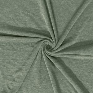 May include: A close-up shot of a sage green fabric with a soft, textured appearance. The fabric is arranged in a spiral pattern, with the center of the spiral in focus. The fabric appears to be a knit or jersey material, suitable for apparel or home decor.