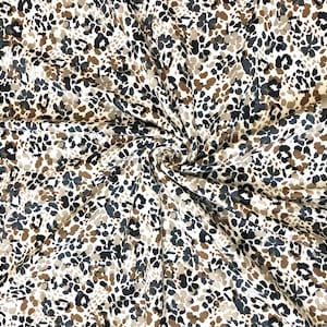 May include: A close-up of a white fabric with a brown and black abstract floral print. The fabric is wrinkled and has a soft, flowing texture.