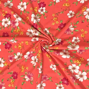 May include: Coral-colored fabric with a repeating floral pattern. The design features white, pink, and burgundy flowers with yellow accents and green leaves. The fabric is gathered in a spiral.