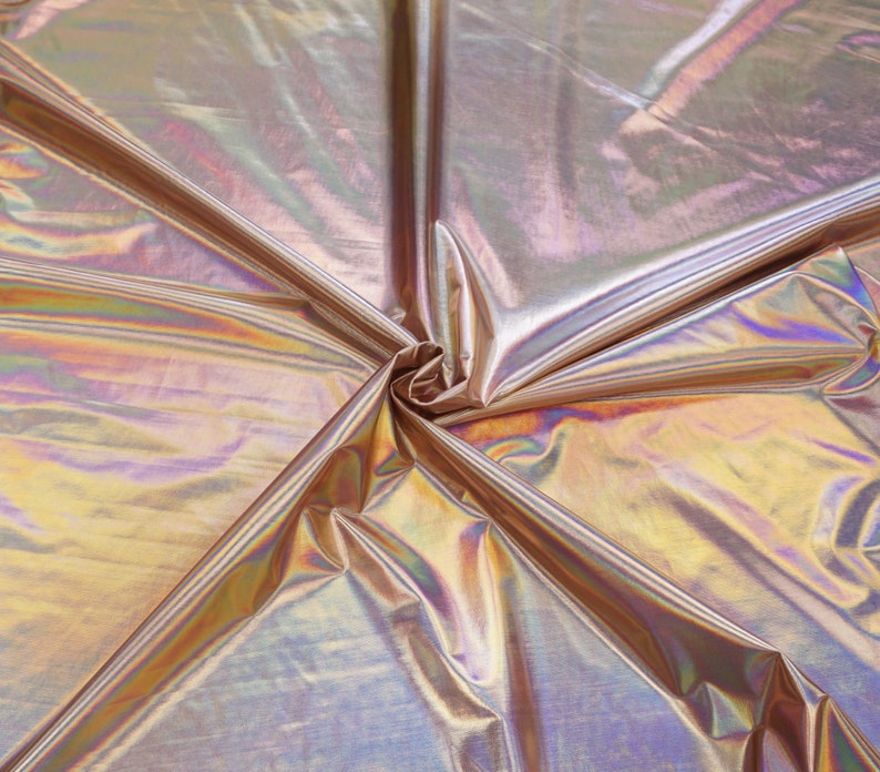 May include: A close-up of iridescent fabric with a metallic sheen. The fabric is folded and draped, creating a swirling pattern of light and shadow.