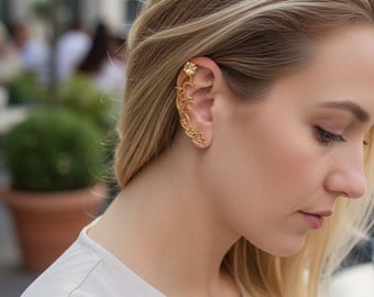 May include: A gold ear cuff featuring a floral design and a small gemstone. The cuff curves along the ear, with a delicate, ornate pattern. The woman in the image is wearing a white blouse.