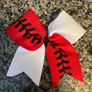 May include: A red and white cheer bow with black glitter baseball stitching.
