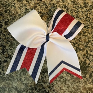 May include: A white cheer bow with red and blue glitter stripes. The bow is tied in a classic cheer bow shape.