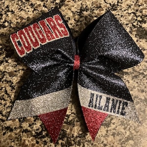 May include: Black, silver, and red glitter cheer bow with the words "Cougar" and "Ailanie" on it.