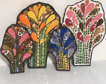 Puede incluir: Cuatro árboles de mosaico hechos de azulejos coloridos, cada uno con un diseño único. Los árboles están dispuestos en una fila de izquierda a derecha, con el árbol más alto en el centro. Los árboles están hechos de diferentes colores y patrones, incluyendo rosa, azul, amarillo y verde.