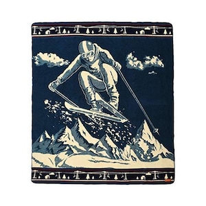 Può includere: Una coperta in pile blu con un disegno bianco di uno sciatore in montagna. Lo sciatore indossa un casco e occhiali da sci e tiene bastoncini da sci. Le montagne sono sullo sfondo e ci sono alberi e uno skilift in primo piano.