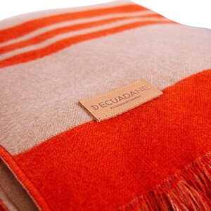 May include: A close-up of a soft blanket with orange and beige stripes. The blanket has a fringed edge and a leather tag that reads "DECUADANE A Lifetime of Comfort."